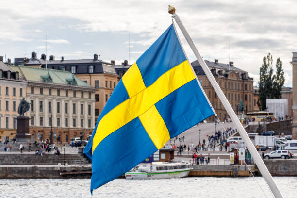 шведский флаг и стокгольм старый город гамла стэн на заднем плане - швеция стоковые фото и изображения