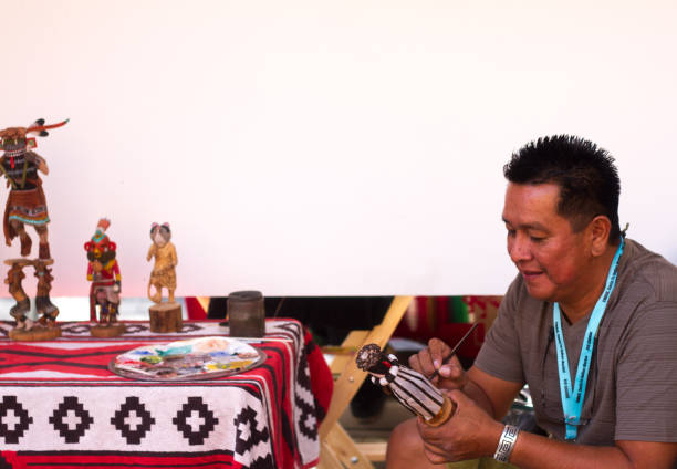 2017 Santa Fe Indian Market: Hopi Sculptor with Kachina Dolls Santa Fe, NM, USA: Hopi artist Brendan Kayquoptewa paints his carved Kachina dolls at the 2017 Santa Fe Indian Market. The market, now in its 96th year, is spread out around the historic Santa Fe Plaza, showcasing North American Indigenous arts and culture. More than 900 artists from hundreds of tribes participate in the two-day event; visitors number about 100,000. kachina doll stock pictures, royalty-free photos & images
