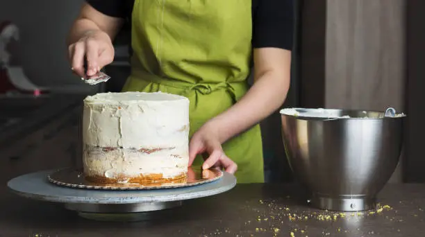 Unrecognisable woman decorating a delicious layered sponge cake with icing cream