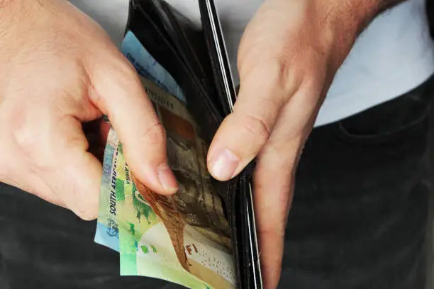 Photo of A man taking South African money out of a leather wallet. This image can be used to represent a cash payment, this image also has selective focusing.