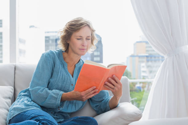 istock Cheerful blonde woman sitting on her couch reading a book 836319644