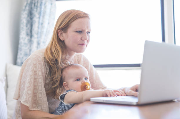 istock Mom works on her computer while holding her infant baby in her lap 836322516