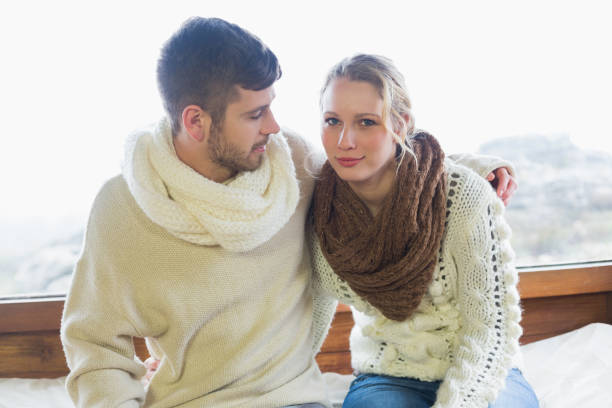 istock Couple in winter clothing sitting against window 836339636