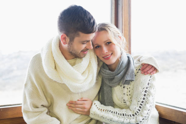 istock Couple in winter clothing sitting against window 836339732
