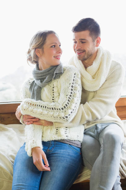 istock Couple in winter clothing sitting against window 836339914