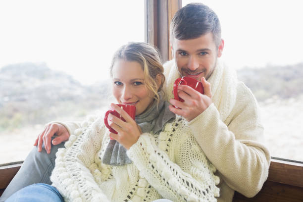 istock Couple in winter clothing drinking coffee against window 836340310