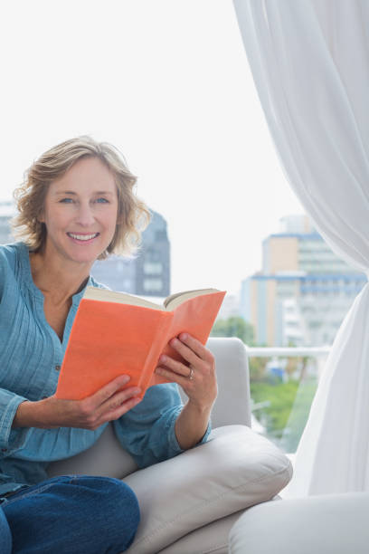 istock Happy blonde woman sitting on her couch holding a book 836346404