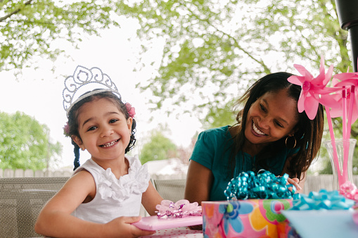 Girl princess tiara opening her gifts with her mother at her birthday party.