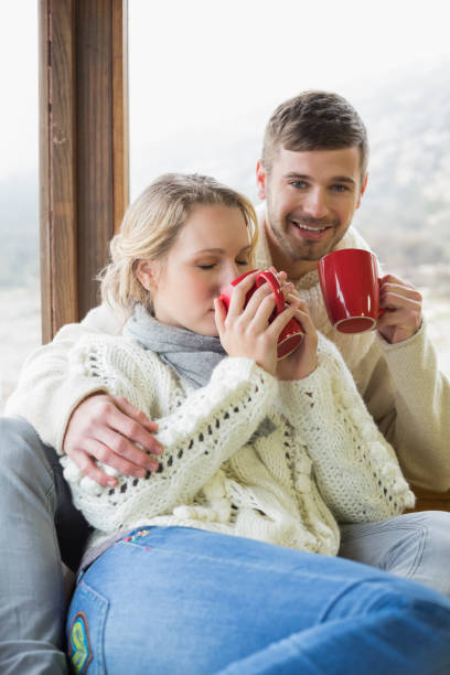 istock Couple in winter clothing drinking coffee against window 836357812