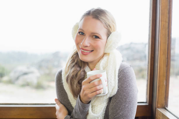 istock Smiling woman wearing earmuff with coffee cup against window 836358322