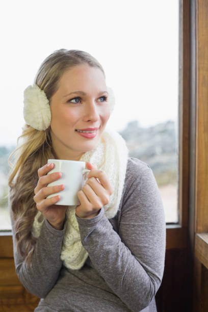 istock Smiling woman wearing earmuff with cup against window 836358444