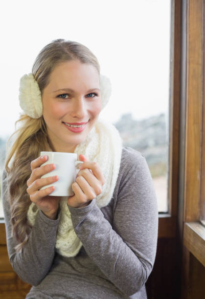 istock Smiling woman wearing earmuff with cup against window 836358456
