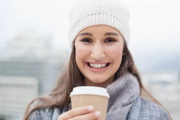 Happy brunette with winter clothes on holding mug of coffee outdoors on a cold grey day