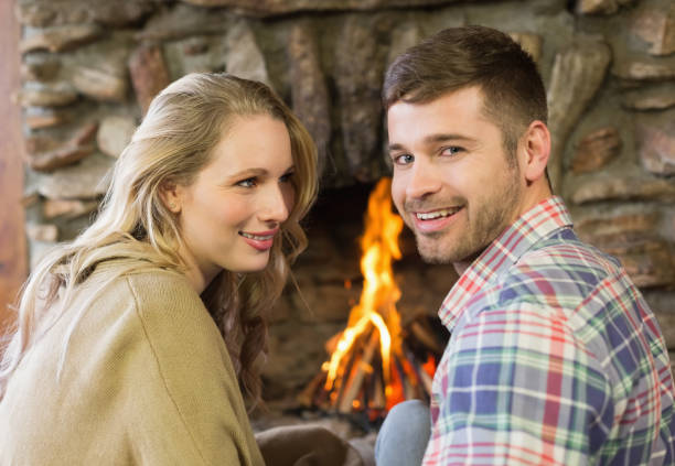 istock Smiling young couple in front of lit fireplace 836372004
