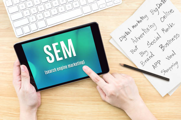 istock Hand using tablet with SEM (Search engine marketing ) word on screen with list of digital marketing features on paper on work table,Online business concept 836372532