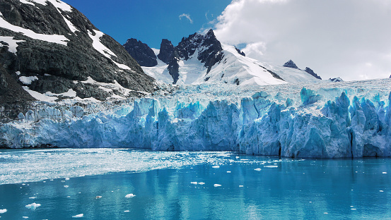 Pieces of floating ice; snow covered mountains with jagged peaks in background.