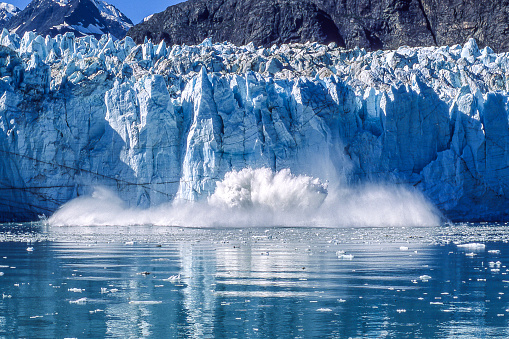 Distant view of tidewater glacier calving into Glacier Bay National Park, with large splashes of water and ice.