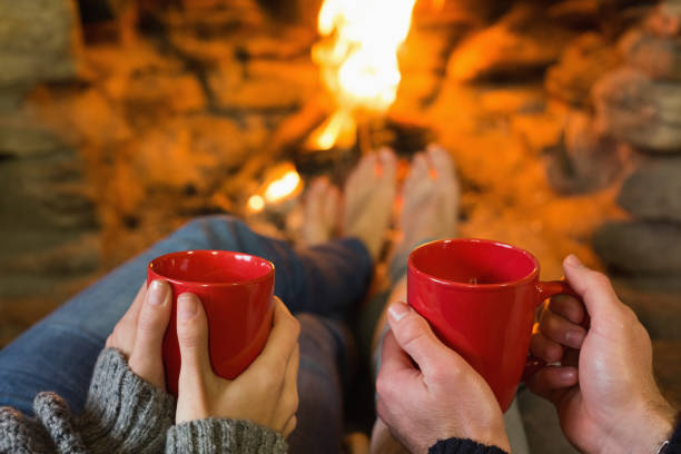 istock Hands with red coffee cups in front of lit fireplace 836383308