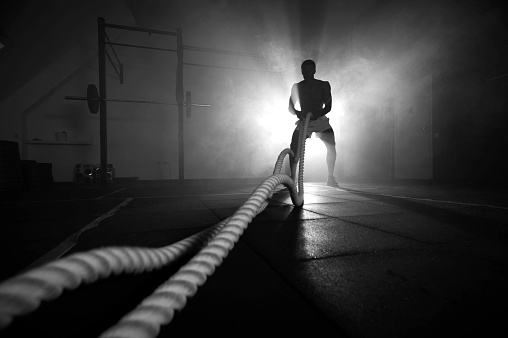 Silhouette of man working out with battle ropes at gym. Functional training. Sports and fitness concept.