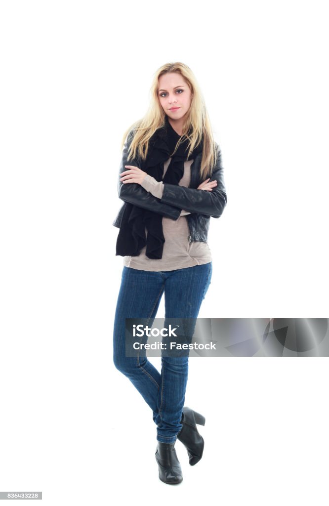 portrait of a blonde model wearing leather jacket and casual clothes portrait of a model with long blonde hair, wearing leather jacket and blue jeans, standing pose against a white background. One Person Stock Photo