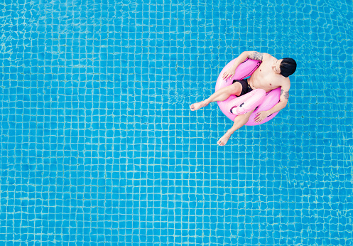 Top view, a man relaxing on pink flamingo swim pool float, on swimming pool in summer