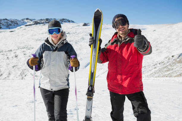 Portrait of a smiling couple with ski equipment on snow Portrait of a smiling couple with ski equipment standing on snow covered landscape thumbs up for skiing stock pictures, royalty-free photos & images