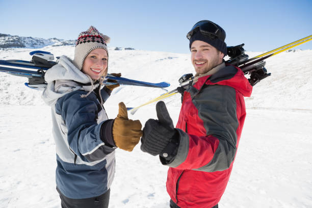 Smiling couple with ski boards gesturing thumbs up on snow Rear view portrait of a smiling couple with ski boards gesturing thumbs up on snow covered landscape thumbs up for skiing stock pictures, royalty-free photos & images