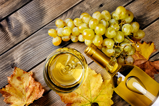 Top view of a glass of wine and fresh bunch of white grapes on a rustic table in aged wood.