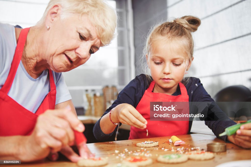 Grandma with girl applying icing on cookies Grandmother Stock Photo