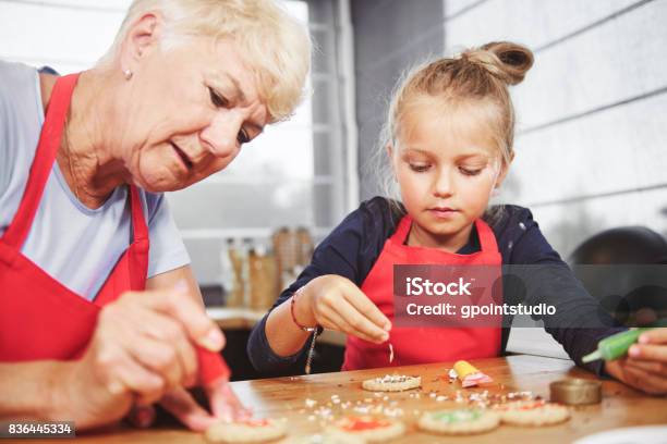 Grandma With Girl Applying Icing On Cookies Stock Photo - Download Image Now - Grandmother, Cookie, Holiday - Event