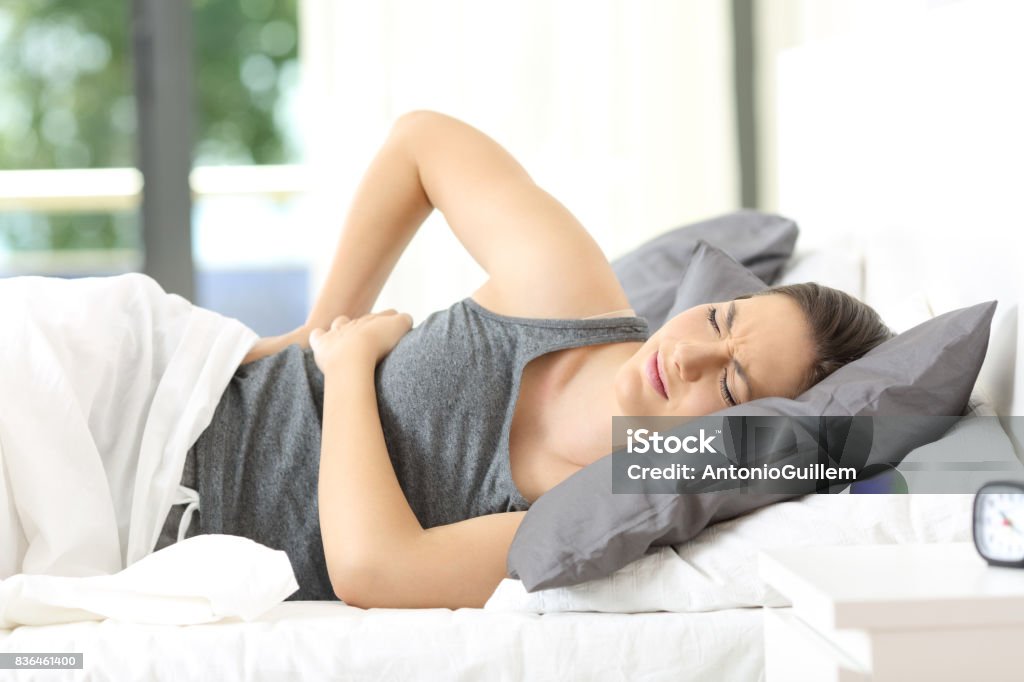 Woman waking up suffering back ache Woman lying on a bed waking up suffering back ache at home or hotel room Pain Stock Photo