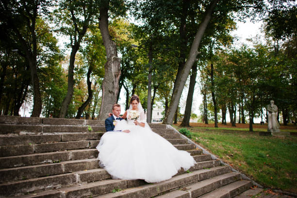 istock Outstanding bride sitting on her husband's lap during their wedding walk in the park. 836470134