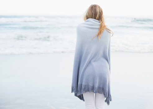 Rear view of a blonde woman warming up in a blanket on the beach