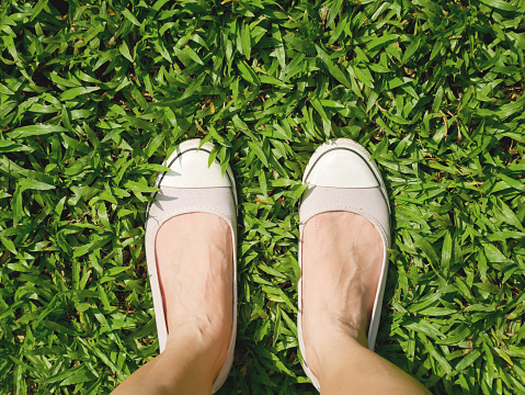 Woman's feet in slip-on shoes standing on the lawn