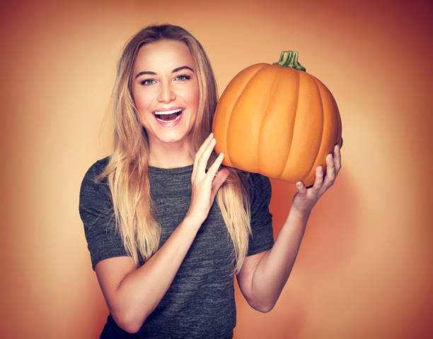 Portrait of beautiful cheerful woman with pumpkin over orange background, celebrating happy Thanksgiving day