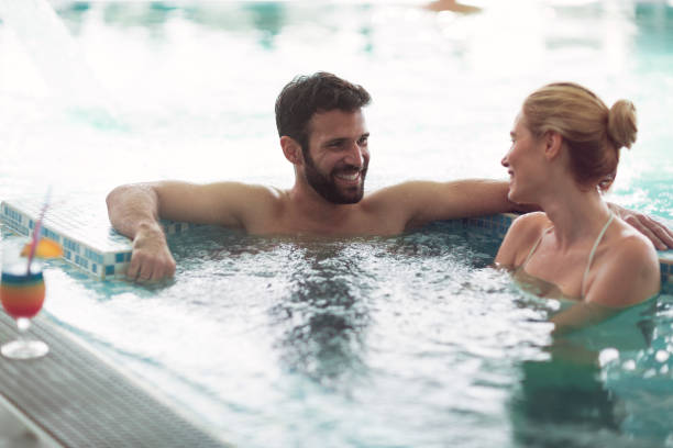 Cheerful happy couple relaxing in swimming pool Cheerful happy couple enjoying together in swimming pool at spa center women exercising swimming pool young women stock pictures, royalty-free photos & images