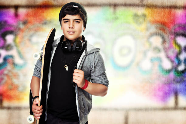 Active teenager with a skateboard, colorful urban graffiti wall background, enjoying outdoors sport, stylish hipster look