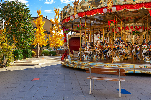 Bench in front of Merry-go-round with horses as trees with yellow leaves on background in autumn in Alba, Italy.