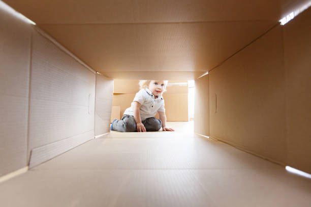 Young happy family moves into a new apartment. Little baby looking into a cardboard stock photo