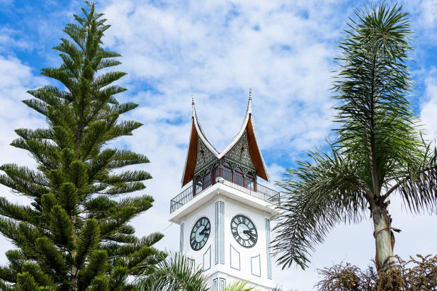 The Jam Gadang Big Clock Tower in Bukittinggi, Sumatra, Indonesia. A major landmark framed by tropical trees.