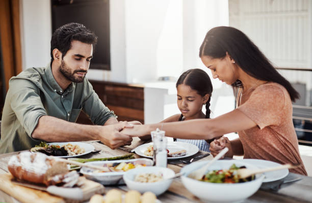 Bless this food and our family Shot of a young family holding hands in prayer before having a meal together outdoors saying grace stock pictures, royalty-free photos & images