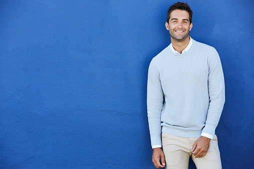 Smiling man in blue sweater against blue wall, portrait