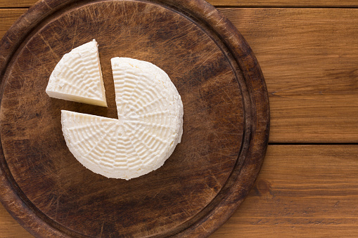 Cheese wheel, fresh homemade indian paneer on wooden board, top view with copy space