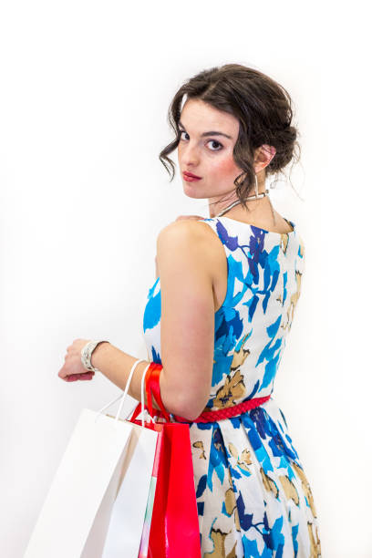 Brunette model looking over shoulder holding shopping bags. Standing with bright summer dress and white background.