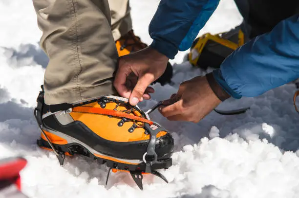 The mans hands professional guide helps you set up and dress alpinist crampons for a beginner mountaineer before climbing