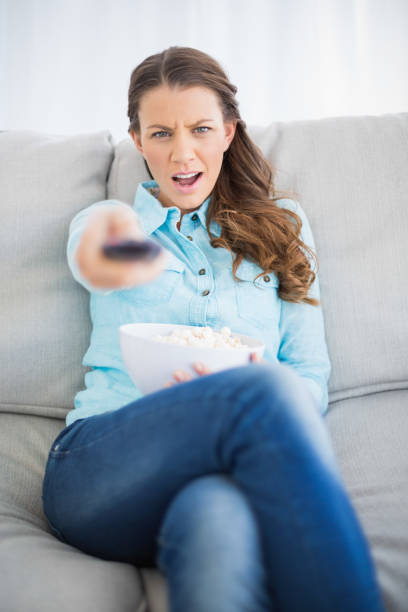 istock Doubtful woman sitting on sofa changing tv channel 836535704