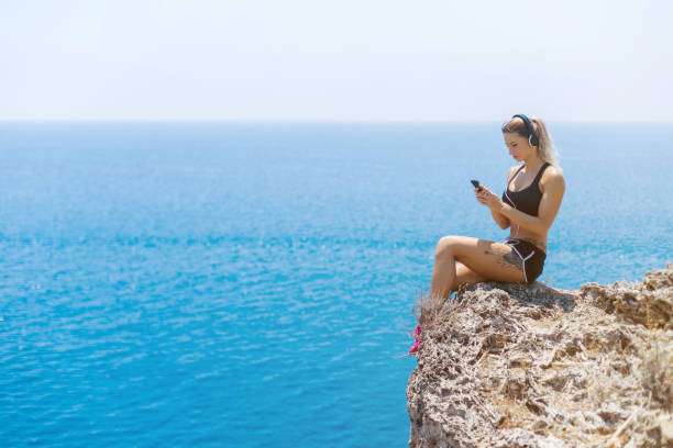 istock Young woman sitting on stone and using smart phone 836538838