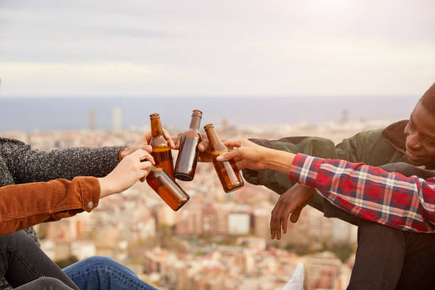 Cropped image of friends toasting beer bottles against cityscape. Men and women are enjoying drinks on building terrace. They are wearing casuals.