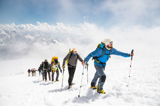 A group of mountaineers climbs to the top of a snow-capped mountain stock photo
