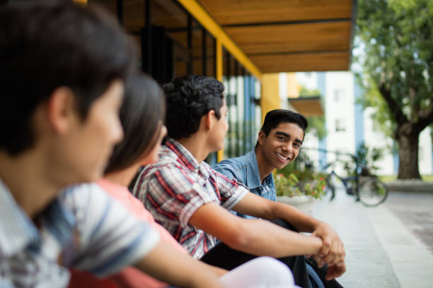 A male college student smiling at the camera and sitting with friends outside.